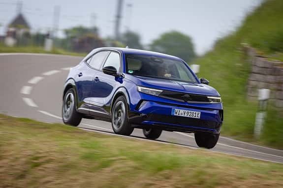 Opel Mokka in blauer Lackierung fährt dynamisch auf einer Landstraße durch eine Kurve.