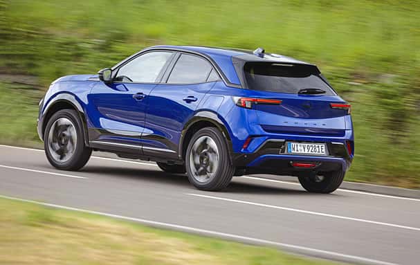 Opel Mokka in blauer Lackierung fährt auf einer Landstraße, fotografiert von schräg hinten.