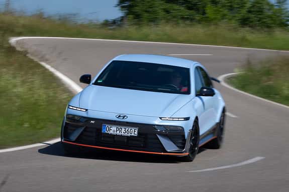 Hyundai Ioniq 6N AWD auf Landstraße in Kurvenfahrt, Frontansicht, sportliche Limousine, hellblau.