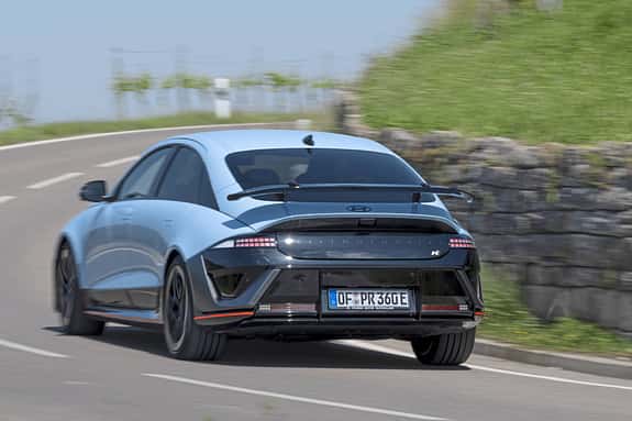 Hyundai Ioniq 6N AWD fährt auf einer Landstraße, fotografiert von hinten, mit sportlichem Heckspoiler.