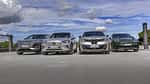 Vier Elektro-SUVs – Audi Q6 SUV e-tron quattro, BMW iX3 50 xDrive, Mercedes GLC 400 4matic EQ und Porsche Macan 4S – nebeneinander auf einer offenen Fläche, fotografiert aus niedriger Perspektive, mit Himmel und Wolken im Hintergrund.