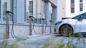 MAHLE charge BIG, MAHLE Smallbox, Ladesäule, Elektroauto, Ladestation, E-Mobilität, Ladeinfrastruktur, Gebäude, Parkplatz, Elektromobilität Mehrere MAHLE charge BIG und Smallbox Ladesäulen für Elektrofahrzeuge vor einem modernen Gebäude, ein Elektroauto ist angeschlossen.