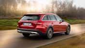 Mercedes C220d 4matic All-Terrain in Rot fährt auf einer Landstraße, fotografiert von schräg hinten, unscharfer Hintergrund.