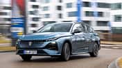 Peugeot e-308 SW 156 PS fährt auf einer städtischen Straße vor modernen Gebäuden.