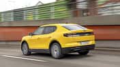 Gelber Ford Capri Extended Range 79kWh fährt auf einer Straße, fotografiert von hinten in Bewegung.