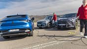 Drei Plug-in-Hybrid-SUVs (Renault Rafale Hyper Hybrid E-Tech, BMW X1 xDrive 30e, Cupra Terramar VZ e-Hybrid) werden auf einem Parkplatz geladen. Zwei Personen in roten Jacken hantieren mit Ladekabeln.