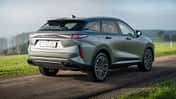Das Bild zeigt einen OMODA 9 SUV in silberner Lackierung, fotografiert von schräg hinten im Außenbereich auf einer Landstraße. Das Fahrzeug steht auf einer asphaltierten Straße, im Hintergrund ist eine grüne Wiese und eine Baumreihe zu sehen. Die Aufnahme hebt das moderne Design und die markanten LED-Rückleuchten des OMODA 9 hervor.