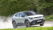 Suzuki e-Vitara eAxle, Suzuki SUV, Elektro-SUV, eAxle, Crossover, Elektroantrieb, 2024, Allradantrieb, Automobil, Fahrdynamik Suzuki e-Vitara eAxle SUV fährt dynamisch auf einer Landstraße, im Hintergrund grüne Vegetation.