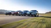 Vier Mittelklasse-SUVs – Mercedes GLC 220d 4Matic, BMW X3 xDrive 20d, Alfa Romeo Stelvio 2.0 Diesel und VW Tiguan 2.0 TDI – fahren nebeneinander auf einer Landstraße.