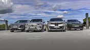 Vier Elektro-SUVs – Audi Q6 SUV e-tron quattro, BMW iX3 50 xDrive, Mercedes GLC 400 4matic EQ und Porsche Macan 4S – nebeneinander auf einer offenen Fläche, fotografiert aus niedriger Perspektive, mit Himmel und Wolken im Hintergrund.